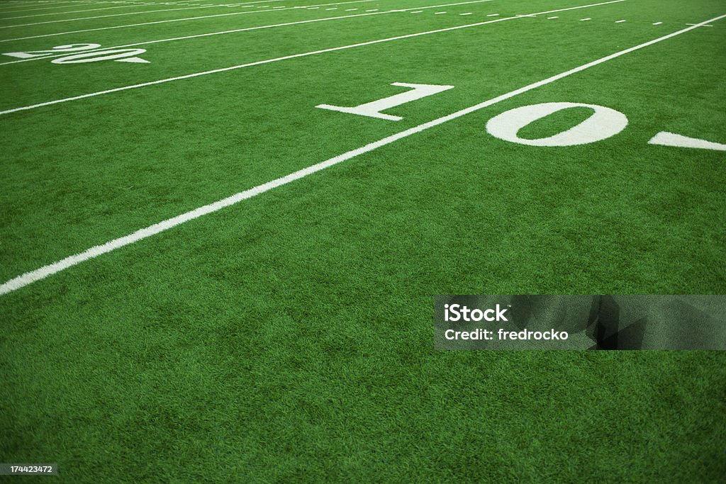 American Football Field and Football Players during a Football Game This color image is of an American Football Field at Football Game. the football field shows the sidelines and each yard-line of the football field. the lawn is green grass or artificial turf. the lighting is natural sunlight during the day.  American Football - Sport Stock Photo