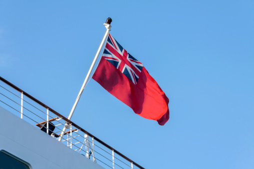 The British Red Ensign flag flying from the rear of a Merchant ship, set against a clear blue sky.