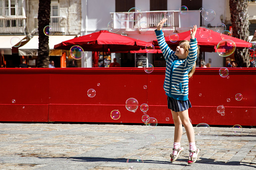 little girl playing on the street with blowing soap bubbles. Happy child in the city