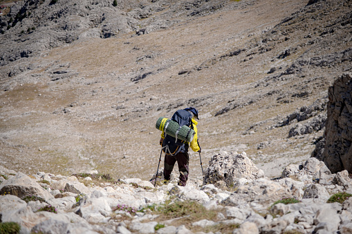 63-year-old fully equipped hiker with a backpack. Baton in hand, backpack on his back. He is descending in extreme terrain. Shot from the arc angle. Mountainous region