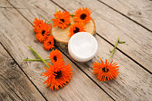 Medical Dermatology. Cosmetic cream for cleansing the skin with calendula flowers. Cream for body care with calendula. Fresh orange calendula flowers on a wooden background in nature.