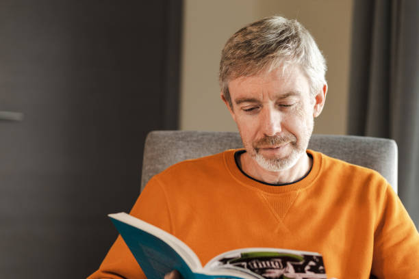 istock 50 year old man sitting in a armchair reading a book 1744305567