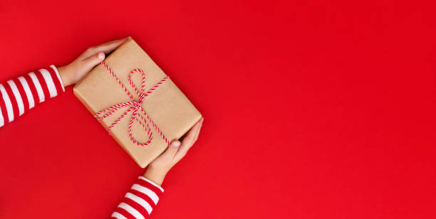istock Christmas banner gift box in children's hands on a red background, presenting a gift 1744306226