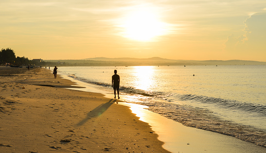 Mui Ne, Vietnam - May 17, 2018. A young man walking on beautiful sunrise beach in Southern Vietnam.