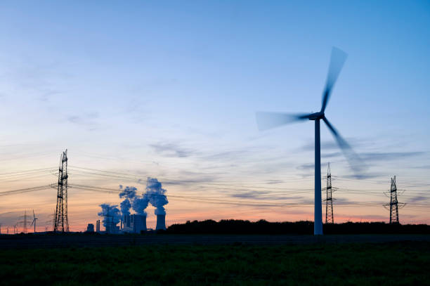 Single wind turbine, a coal burning power plant and electricity pylons in the background.