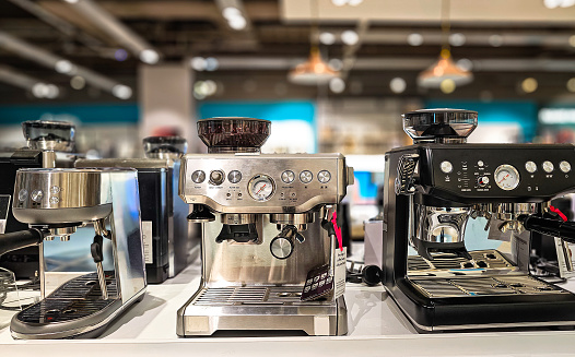 Modern coffee machines on display and for sale in the department store. Focus on the machines with the store defocused beyond.