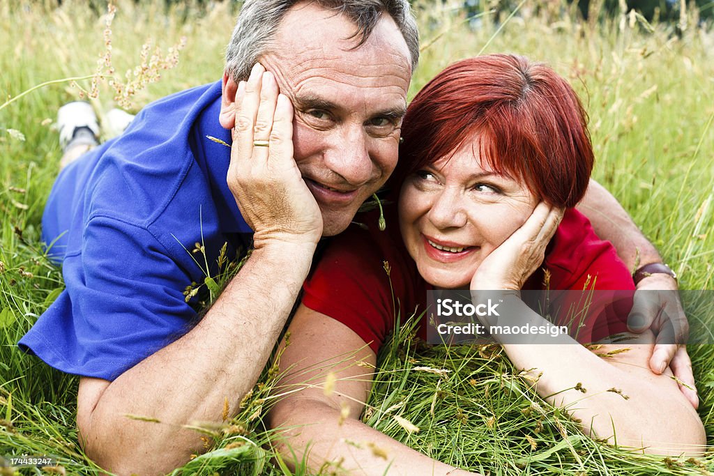 Happy Mature Couple Lying on Grass Embracing, Portrait A happy mature couple embracing, lying on their stomachs in a meadow. 50-54 Years Stock Photo