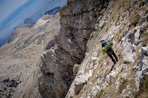 63-year-old fully equipped hiker with a backpack. Baton in hand, backpack on his back. He is descending in extreme terrain. Shot from the arc angle. Mountainous region