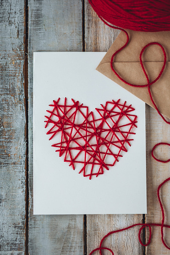 Handmade gift greeting postcard from recycled paper with embroidering with red woolen heart. Saint Valentine's day diy, wedding or other holiday romantic decor on wooden background.