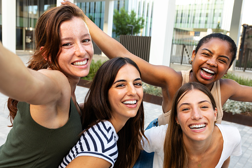 Selfie portrait of happy young girl friends looking at camera excited. smiling group of multiracial women having fun together outdoors. Piggyback. Female friendship concept.
