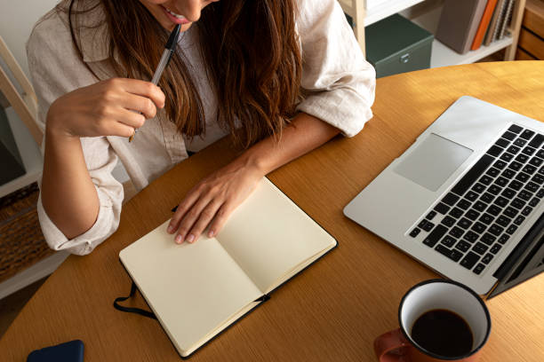 istock Top view of unrecognisable young woman planning handwriting on notebook while working at home office. 1744356407
