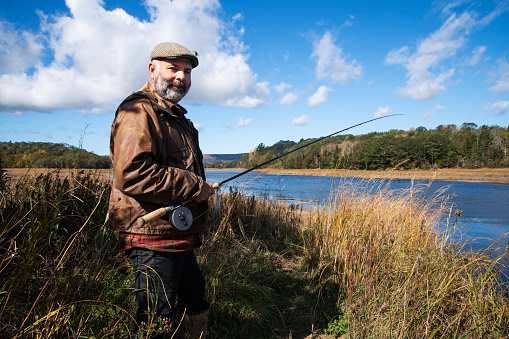 A fly fisherman beside a river estuary on a beautiful autumn day