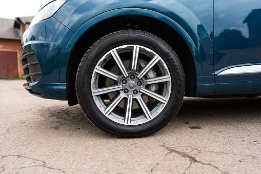 Vehicle tire of auto model in firmament blue metallic color parked in urban area. Main purpose of limiting transmission of road vibrations to automobile body. High quality photo