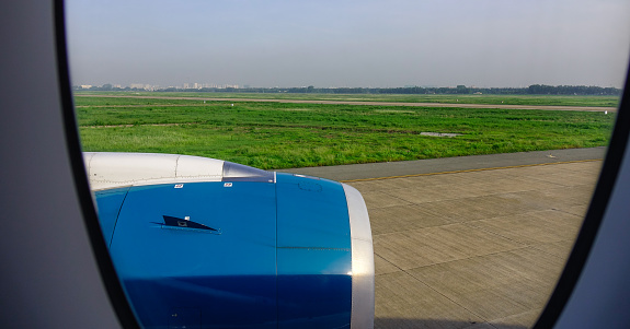 Saigon, Vietnam - Jun 3, 2019. Window with blue engine of passenger airplane at the Tan Son Nhut airport.