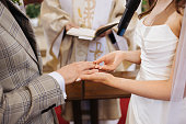 Wedding ceremony background. Catholic church ceremony. Vow moment. Bride putting ring on groom finger.