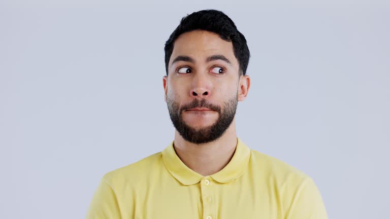 Face, guilty or awkward with a man in studio on gray background looking nervous or uneasy. Autism, doubt or adhd with an embarrassed young person thinking of an idea while feeling confused or unsure