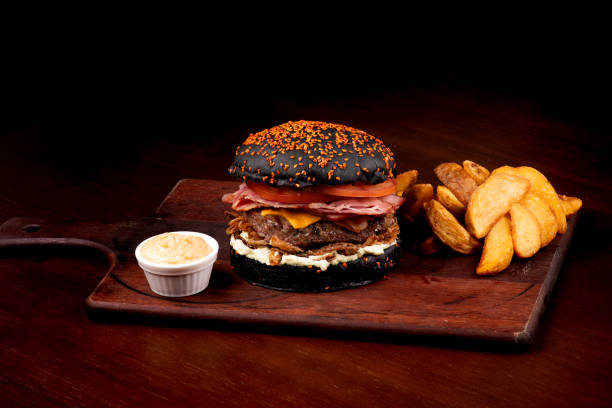 istock juicy classic burger with halloween themed black sesame seed bun with cheddar bacon crispy onion tomato rustic potatoes on wooden board 1744457712