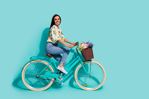 Full length photo of lovely pretty girl wear stylish outfit having fun riding bicycle empty space isolated on bright cyan color background.
