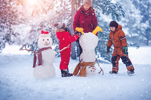 Family building a cute snowman in the snowy park. Concept of the family vacation and weekend together.