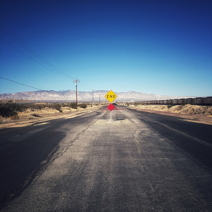 An evocative scene captures a deserted road in a vast, arid landscape. Dominated by a bold yellow 