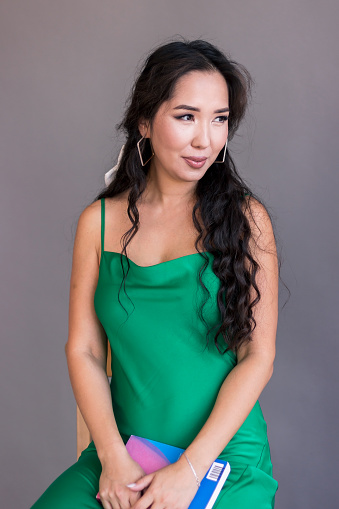 Portrait of happy young beautiful asian woman in green dress smiling and holding the book in the hands.