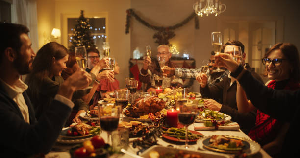 istock Christmas Evening Celebration at Home with Multicultural Group of Loved Ones Enjoying a Turkey Dinner. Old and Young Family Members Raising and Clinking Glasses to Celebrate a Festive Occasion 1744498953
