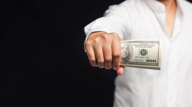 istock Businessman in a white shirt holding US dollar bills while standing on a black background 1744500586