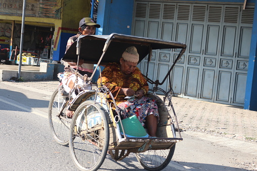 Brebes-Indonesia, 27 January 2020. A rickshaw puller is pedaling his rickshaw with an old female passenger.