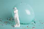 a venus in front of a balloon of the same color as the background and confetti