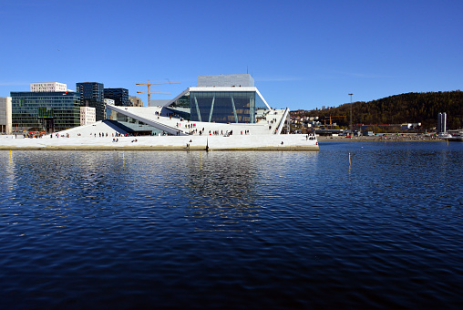 Oslo, Norway: office buildings and the opera house reflected on the waters of Bjørvika Bay - The building, a two-part theater with opera and ballet, was modeled on a floating iceberg, was designed and built by the Norwegian architectural firm Snøhetta (“Snow Cap”), famous for the new library of Alexandria in Egypt - with Christoph Kapeller as design leader and project director - Bjørvika neighborhood in the Sentrum borough, named after Bjørvika bay.