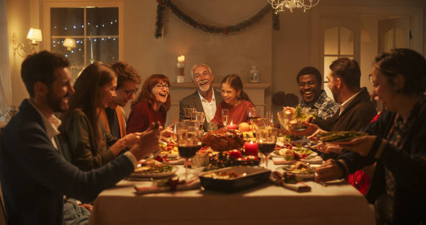 les membres de la famille multigénérationnelle partagent des histoires drôles et de la joie lors d’un dîner de dinde de noël. des parents et des enfants heureux chantent des chants de noël ensemble, dansent derrière une table et allument des étin - dining senior adult friendship mature adult photos et images de collection