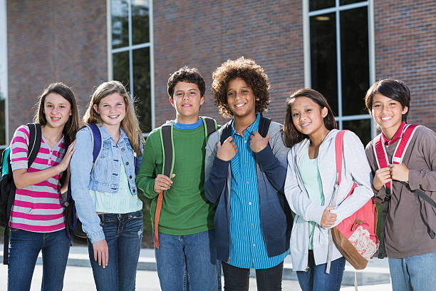 Students standing outside building Multi-ethnic group of students standing outside school building. boy and girl looking at camera stock pictures, royalty-free photos & images
