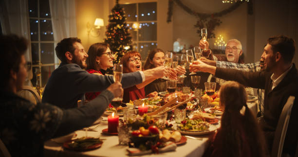 porträt eines gutaussehenden jungen schwarzen mannes, der an einem weihnachtstisch einen toast ausspricht. familie und freunde essen gemeinsam, stoßen mit champagner an, stoßen an, feiern einen winterurlaub - after dinner stock-fotos und bilder