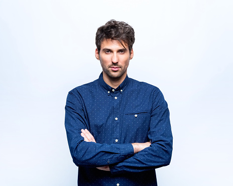 Confident mid adult man wearing navy blue shirt standing with arms crossed and looking at camera. Studio shot.
