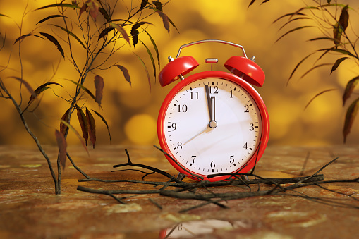 Red alarm clock showing the time 90 seconds to twelve o'clock (midnight) in an autumn scene. Illustration of the concept of doomsday time, impact of climate change and deadline of projects