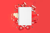 Blank Notepad with White Paper Page against Red Christmas Decorations. Invitation, Wish List Mock-Up. Empty Notebook. Resolutions, plan, goals, checklist, idea concept. Top view. New Year. Xmas banner