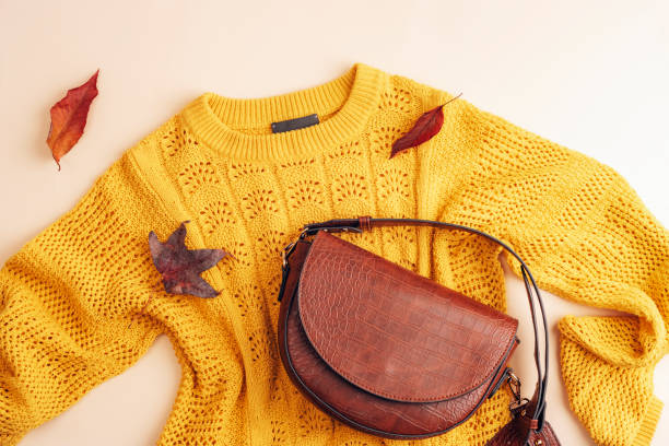 ベージュの背景に女性の黄色いセーターと茶色のバッグの平らな敷物、紅葉。秋のファッションコンセプト。平面図、フラットレイ