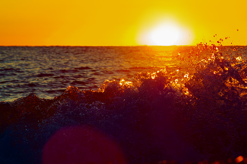 Evening sunset on sea. View of sun over horizon. Splashes of ocean waves. Backlight. Beautiful background.