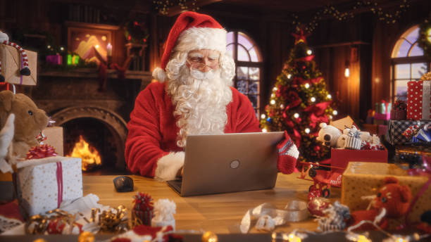 istock Arc Shot of Father Christmas Sitting and Using a Modern Laptop Computer. Santa is Browsing Online, Communicating with Clients, Managing a Successful Online Shopping Business with Gifts for Children 1744549166
