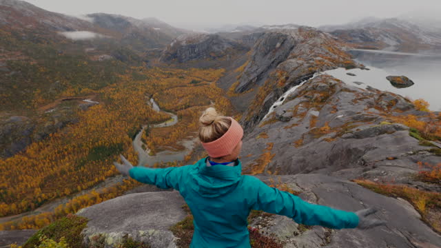Woman hikes in the mountains of Northern Norway, she stands arms outstretched embracing nature