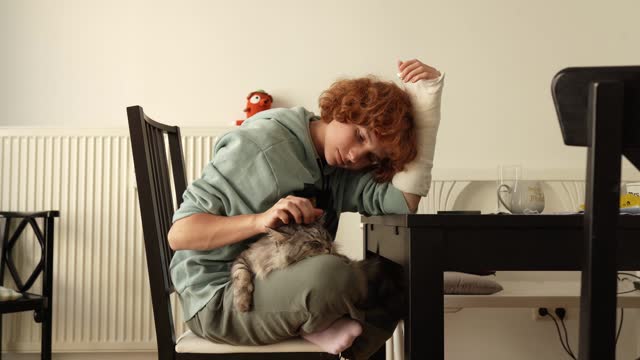 Portrait teenage girl with red hair, cast on arm and domestic cat at home