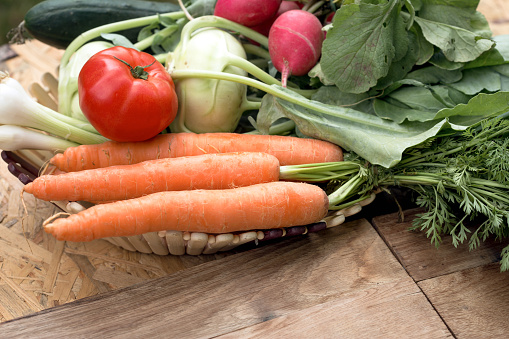 Fresh organic vegetables in a basket on wooden table, healthy vegeterian food close-up