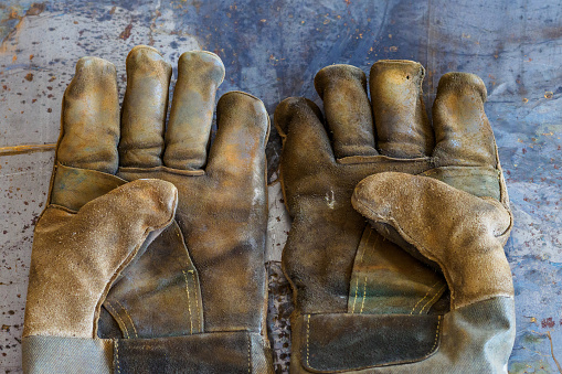 Worn welding gloves lie on table, palms up. Top view of working gaiters. Background.