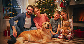 Holiday Portrait of a Loving Family Posing for Camera, Smiling and Hugging Each Other. Boyfriend, Girlfriend, Two Kids and a Pet Dog Sitting in a Festive Living Room with Christmas Tree