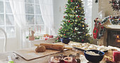 Peaceful Snowy Christmas Morning: Shot of a Table with Baking Ingredients and Utensils in a Decorated Corner of a Modern House with a Christmas Tree, Fireplace and Gifts. Holiday Preparations