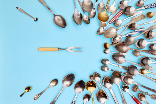 Cutlery. Top view photo one kitchen fork surrounded of variety of antique silverware and gold spoons against blue studio background. Concept of food, holiday, table setting, retro, vintage.