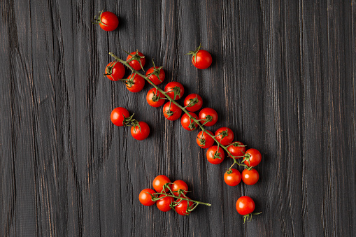 Cherry tomatoes on branches on a dark wooden background, top view. Fresh cherry tomatoes on a textured background. Organic vegetables, veganism.