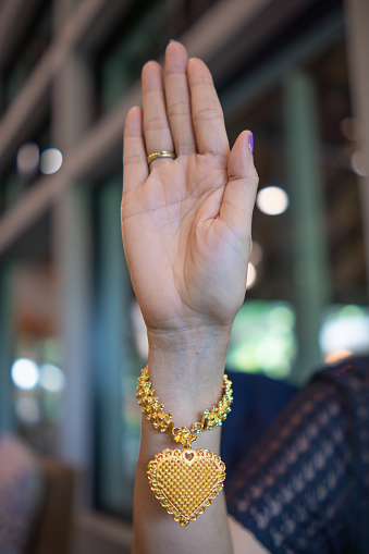 young woman holds up her hand wearing gold heart-shaped bracelet and pendant to greet and symbolizes love and friendship with heart shaped pendant. Concept of symbolizing love, friendship and kindness.
