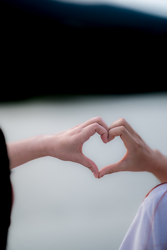 young woman and her friend raised their hands together to form heart shape to show their friendship love and kindness with their belief and power of faith in their friendship. concept of friendship