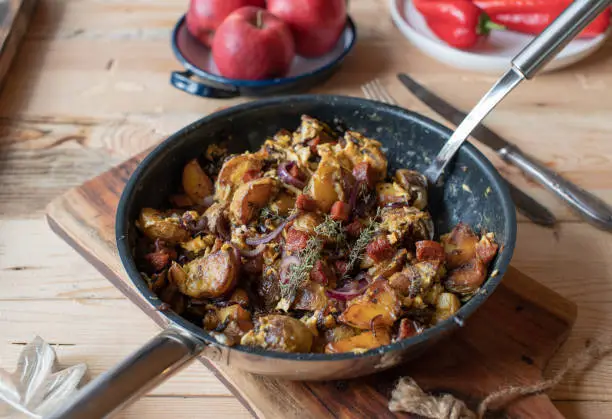 Delicious country food with pan fried potatoes with scrambled eggs, chorizo sausage and red onions in a frying pan on rustic and wooden table background.